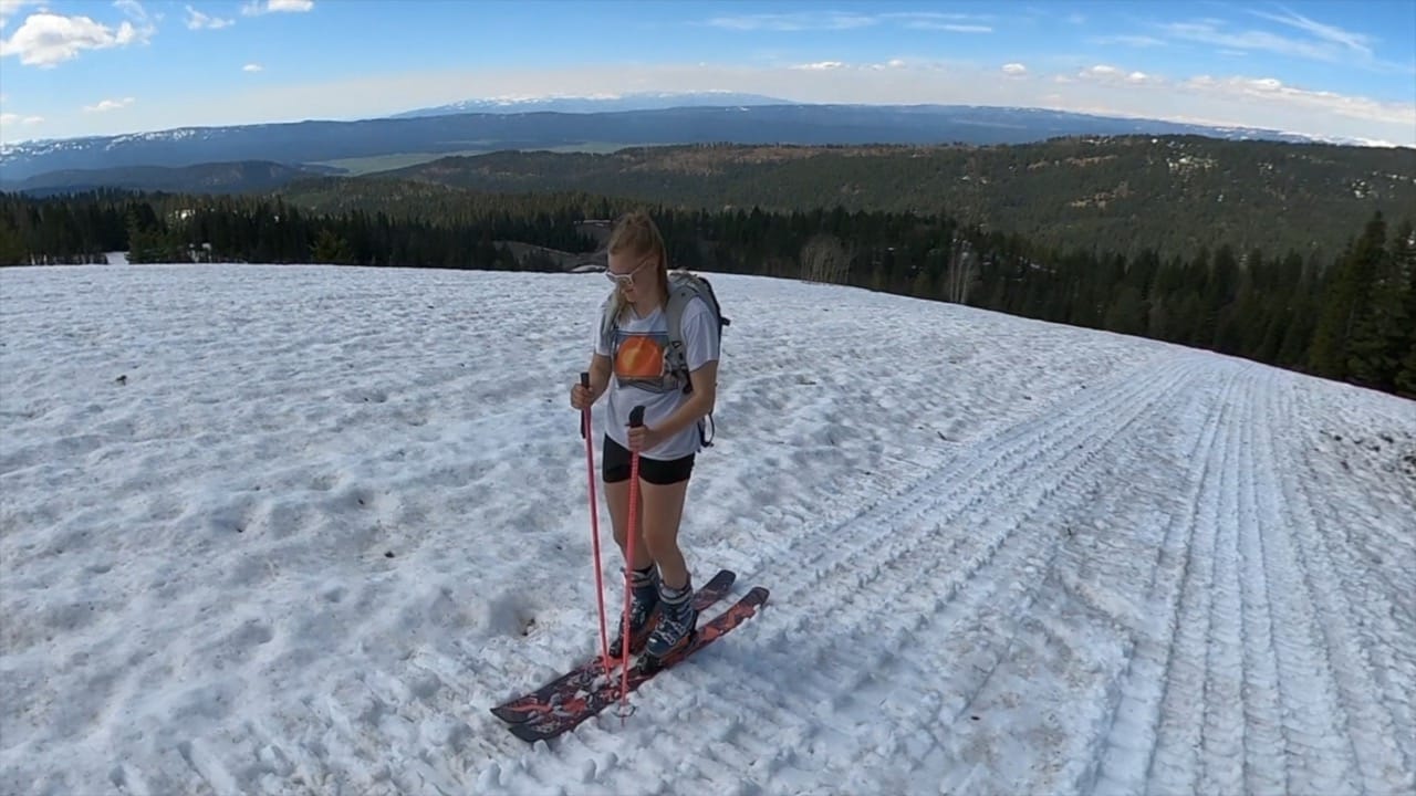Girl in t-shirt and shorts skinning up a ski slope.