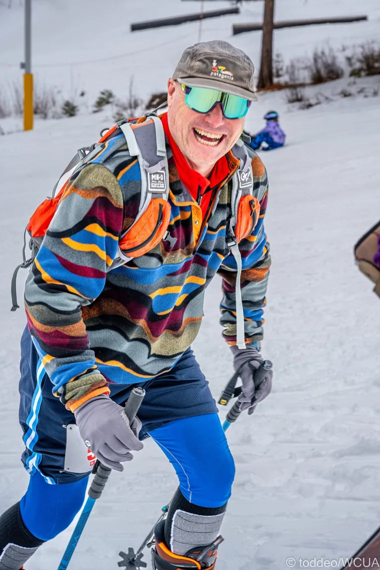 Picture of smiling man skinning up a mountain in a colorful outfit. 
